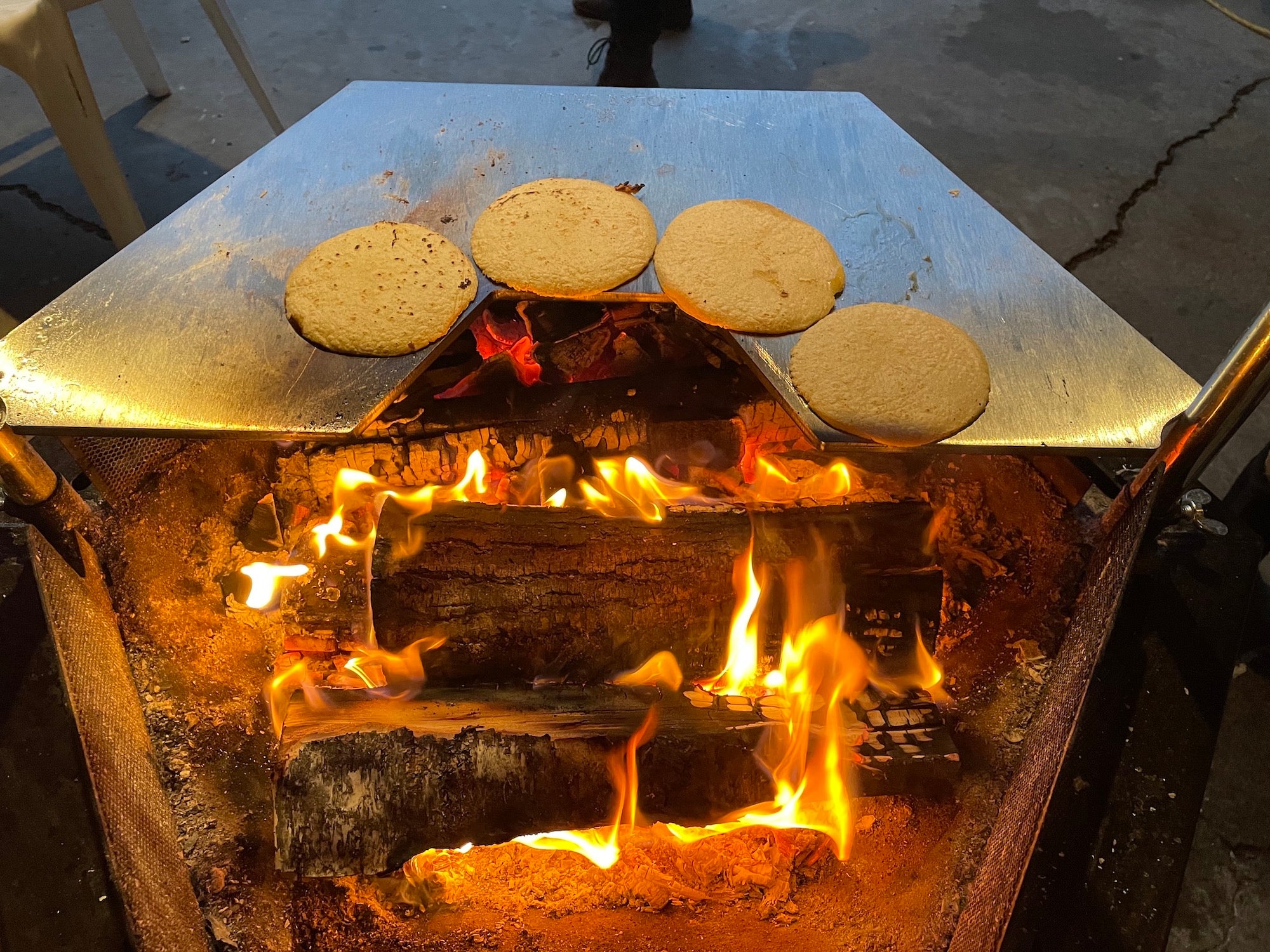 Four tortillas cooking on the Roasting plate accessory on a Kota Grill above a hot wood fire.