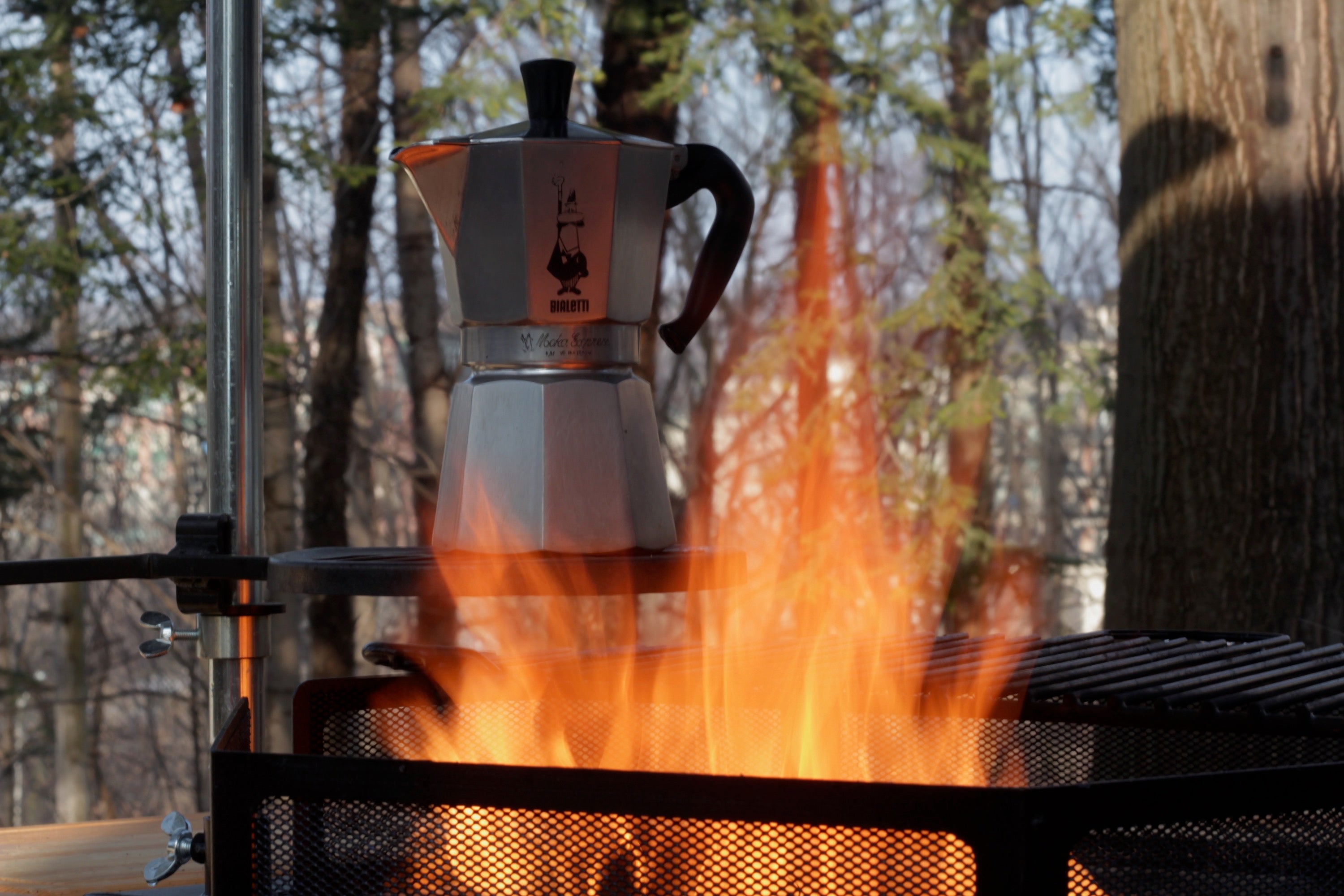 An esspresso pot lapped by fire sitting above a Kota Grill.