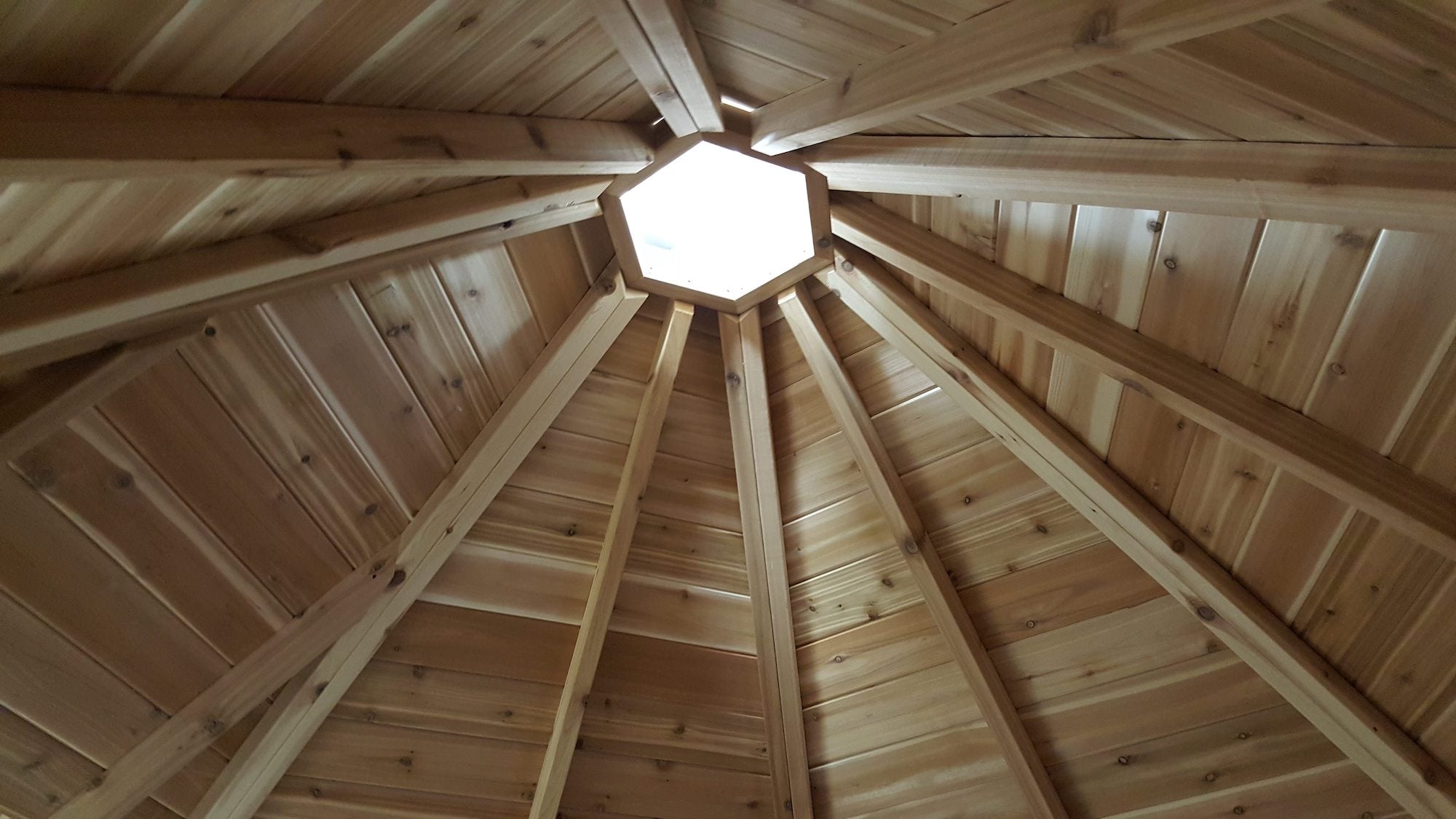 Light shines through the cabin structure, yet to have a chimney installed. Intricate wood-work makes up the ceiling.