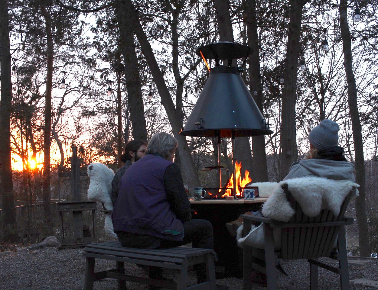 Three people sit around a Kota Grill with coffee at sunset.