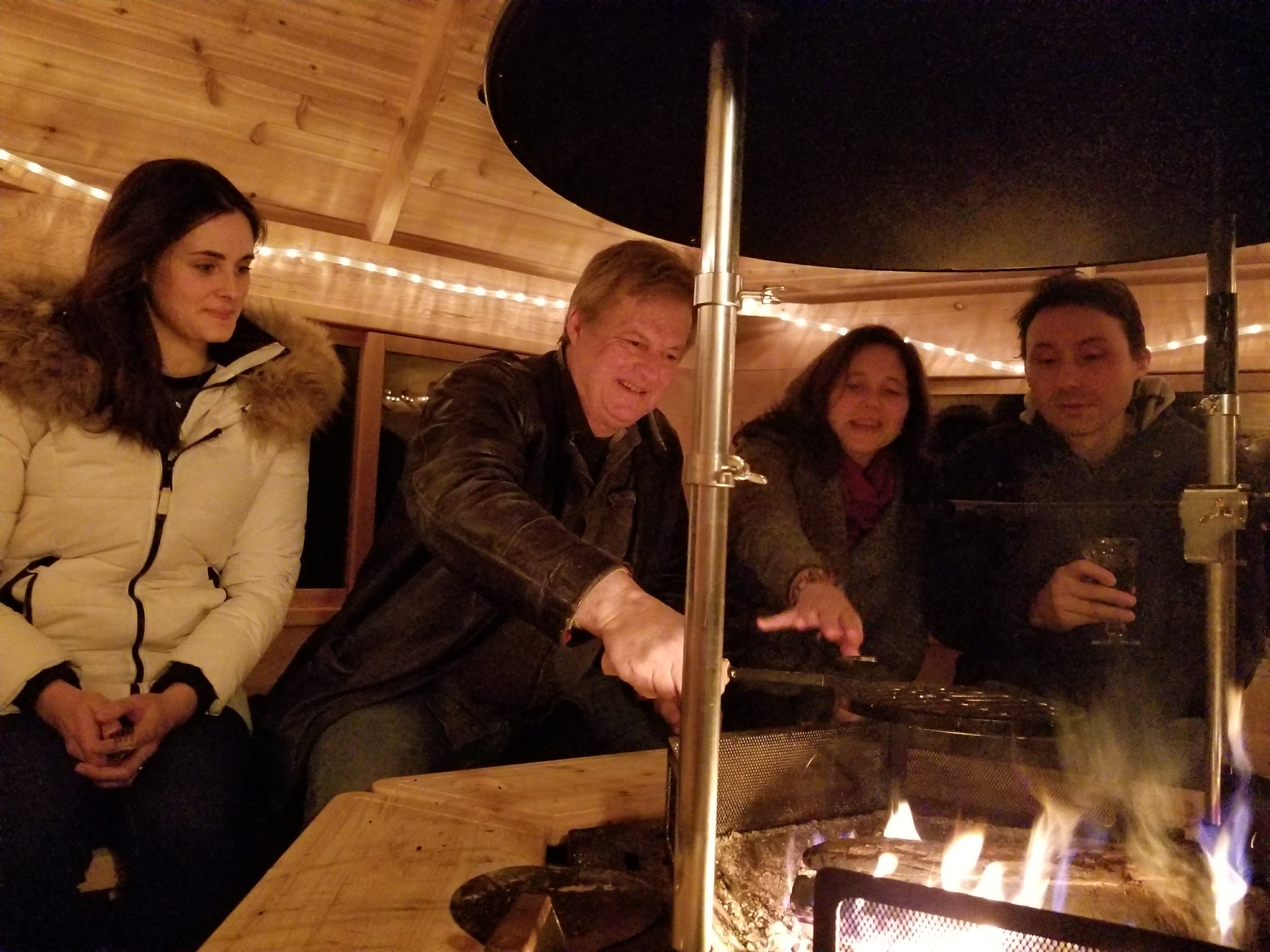 A group of people sit around inside a Kota Cabin looking at the fire.