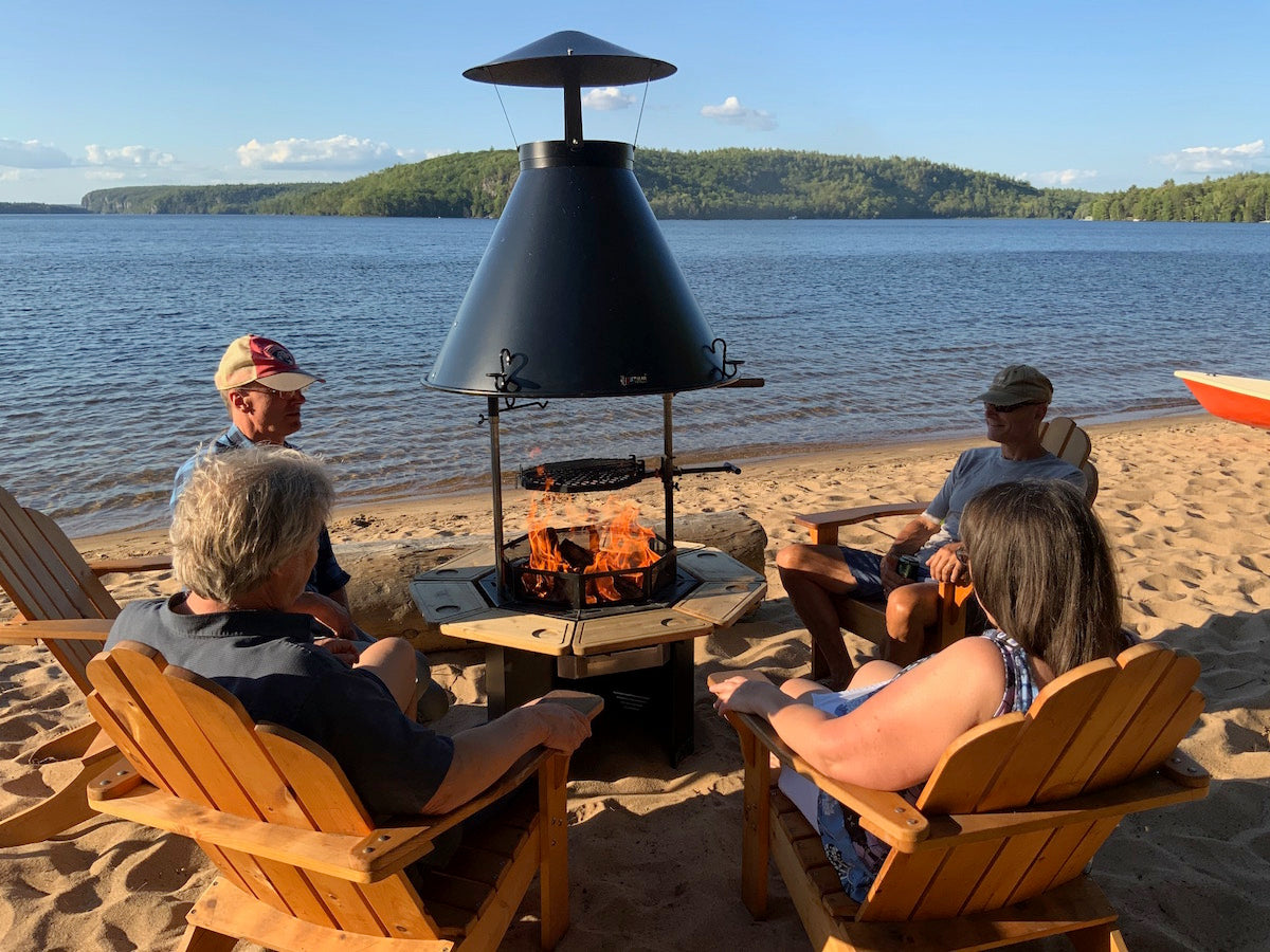 A kota grill sits on a beach with a group of people sitting around it.