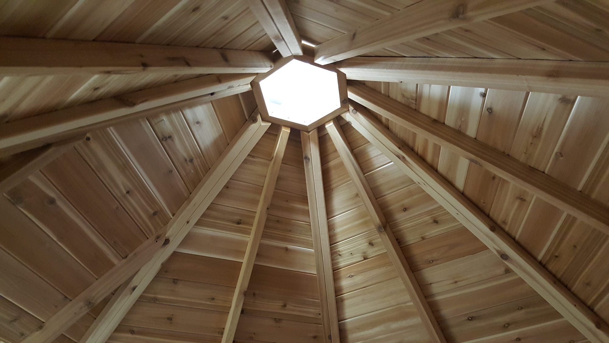      Light shines through the cabin structure, yet to have a chimney installed. Intricate wood-work makes up the ceiling.  